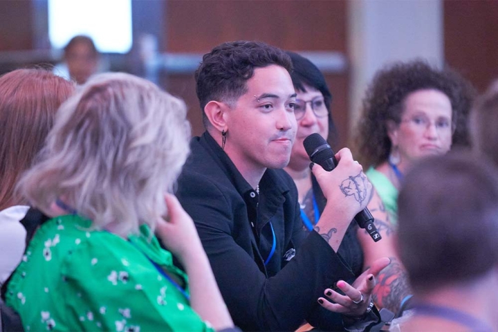 Dillon talking into a microphone at a conference with people surrounding him blurred in the foreground and background