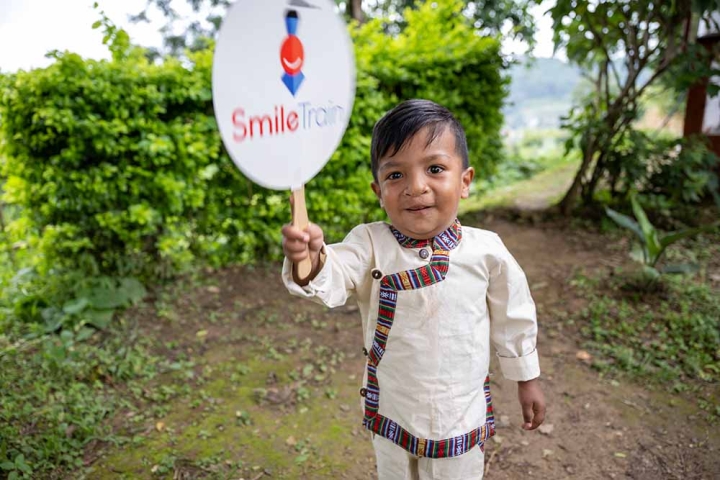 Asher smiling and holding a Smile Train sign