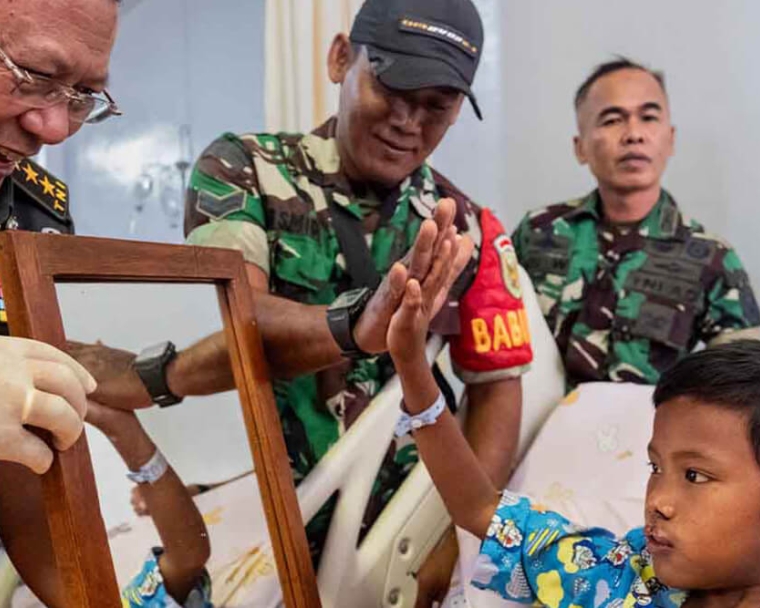 Indonesian soldiers smiling and high-fiving Rajib as he looks at himself in the mirror after his cleft surgery